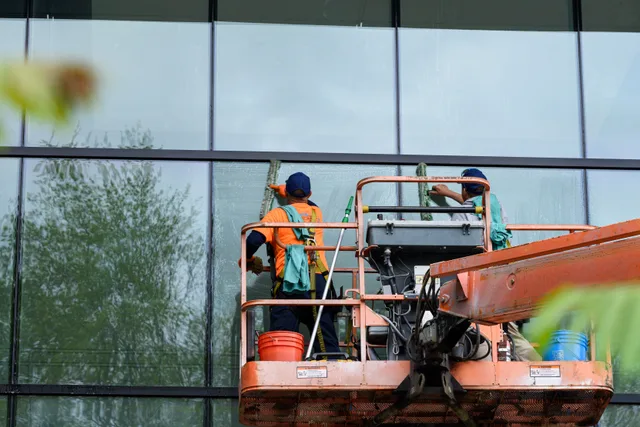 Two workers cleaning windows on a glass building facade using a lift platform, enhancing building aesthetics. Local SEO for a window cleaning business: the checklist