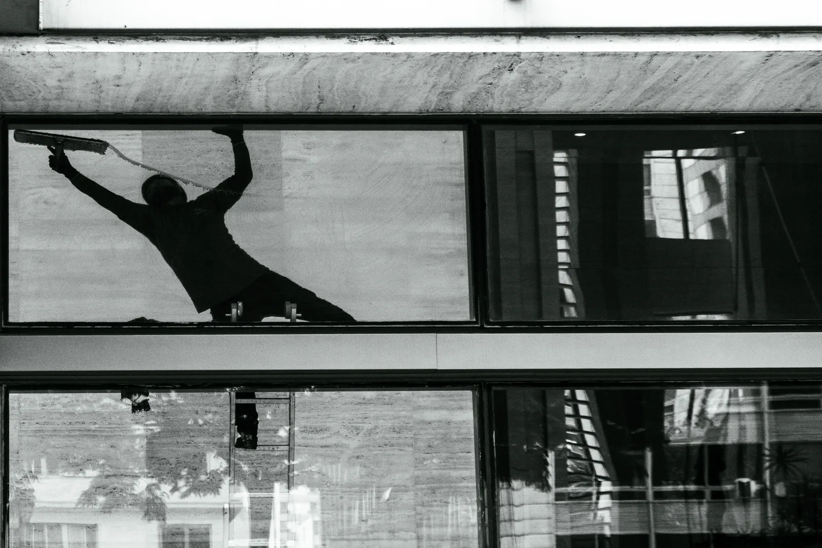 Silhouette of a window cleaner with squeegee on building glass, reflecting urban architecture. Window Cleaning Business in Canada: Sole Proprietorship vs Corporation
