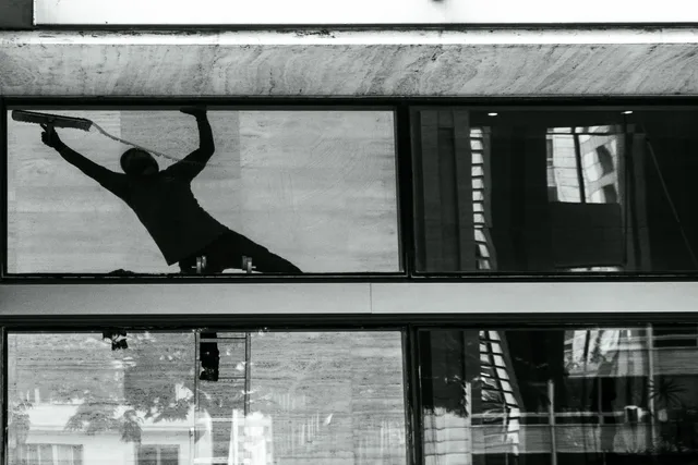 Silhouette of a window cleaner with squeegee on building glass, reflecting urban architecture. Window Cleaning Business in Canada: Sole Proprietorship vs Corporation