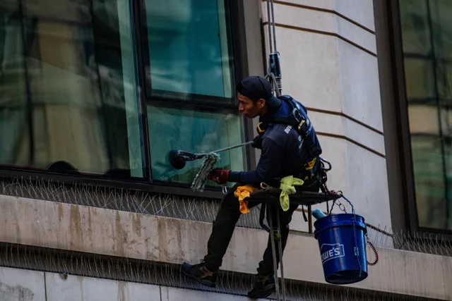 Man cleaning high-rise building windows using safety harness outdoors in daylight. What Window Cleaning Contract Terms Should You Always Include?