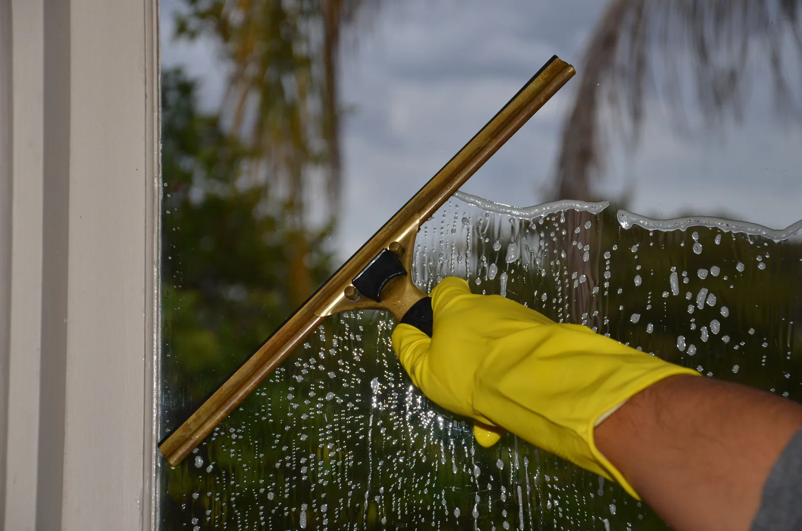 Close-up of hand cleaning window with squeegee outdoors using yellow gloves. Window cleaning equipment checklist: the van, packed in job order