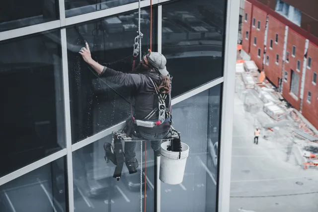 A worker cleaning skyscraper windows with a harness in an urban setting. Window Cleaning Services: Choosing Service Lines