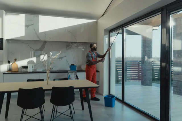 A professional cleaner in uniform washing large glass windows indoors with natural light streaming in. Top window cleaning software, rated on evidence rather than hype